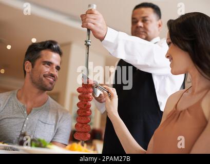 Helping herself to some delicious meat. A happy couple having a meal at a fine dining restaurant. Stock Photo