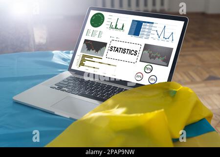 Laptop Computer Showing Statistical Infographics Stands on a Desk in the Living Room. In the Background Cozy Living Room. Stock Photo