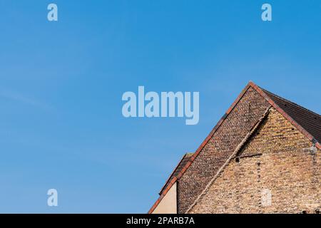 Fragment of an old tiled roof against the blue sky. The building is made of weathered red brick. Stock Photo