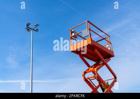 Orang lifting tower climbs up to a street lamp. Against the background of the blue sky. Stock Photo