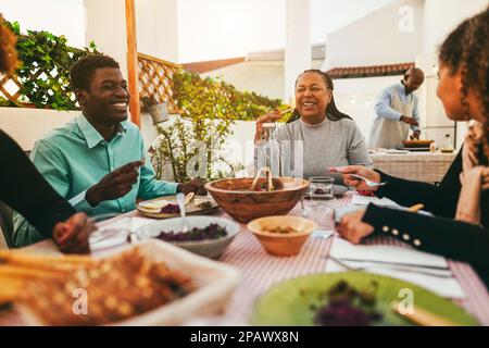 Happy african family eating lunch together at home terrace outdoor - Focus on senior woman face Stock Photo