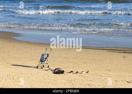 Galveston, Texas, USA - February 2023: Shoes and a pushchair with backpack left unattended on the beach by a family Stock Photo