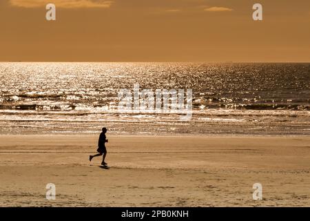 Galveston, Texas, USA - February 2023: Silhouette of a person running along the beach at low tide at dusk Stock Photo