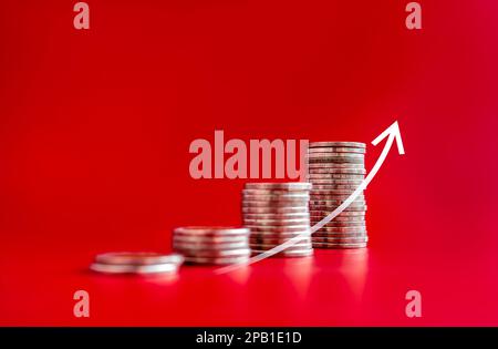 Rising arrow growing on coin stacks as graph chart steps isolated on red background. Investment, saving money, financial income, purchase trend increa Stock Photo