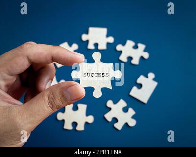 Success concept. Word "SUCCESS" showing on puzzle jigsaw piece holding by business person's hand, choosing from other pieces on blue background. Stock Photo