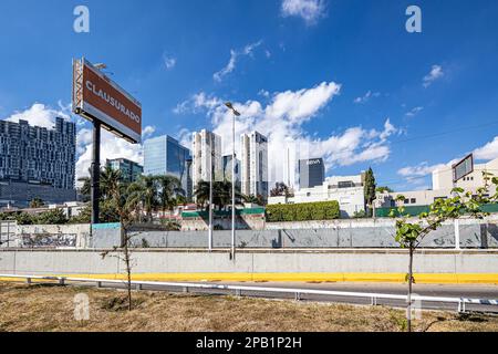 Zapopan, Jalisco Mexico. January 1, 2023. Empty vehicular street with fences and modern buildings against a blue sky on sunny day, spectacular with in Stock Photo