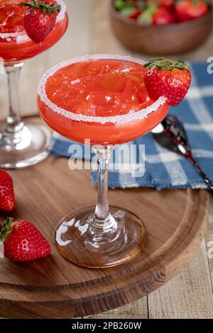 Strawberry margarita cocktail garnished with strawberries and salt rim on a wooden platter Stock Photo