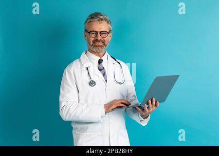 Happy mature european therapist using laptop on blue Stock Photo