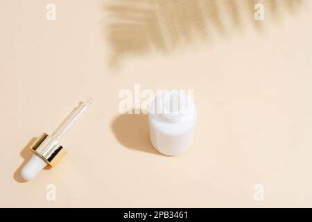 White dropper bottle with pipette and fern leaf shadow on beige background. Natural anti-aging cosmetics concept. Top view. Stock Photo