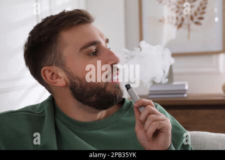 Handsome young man using disposable electronic cigarette at home Stock Photo