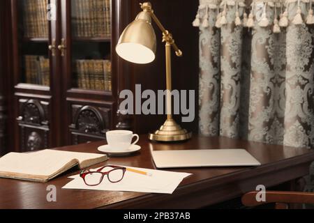 Laptop, book and papers on wooden table in library reading room Stock Photo