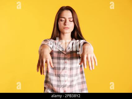 Young woman wearing pajamas in sleepwalking state on yellow background Stock Photo