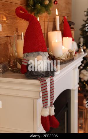 Cute Christmas gnome and festive decorations on mantelpiece in room Stock Photo