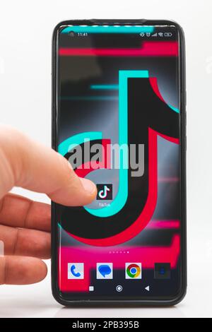 A man's finger points to the TikTok app icon on a smartphone screen on a white background Stock Photo