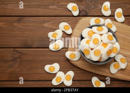Delicious gummy fried eggs shaped candies on wooden table, flat lay. Space for text Stock Photo