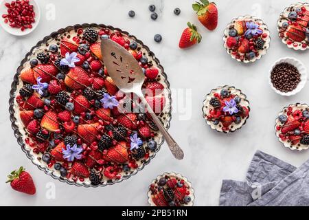 Top down view of a mixed berry cheesecake tart and tartlets to the side. Stock Photo