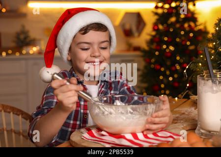 Cute little boy in Santa hat making dough for Christmas cookies at home Stock Photo