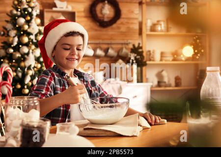 Cute little boy in Santa hat making dough for Christmas cookies at home Stock Photo