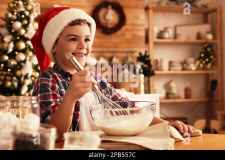 Cute little boy in Santa hat making dough for Christmas cookies at home Stock Photo