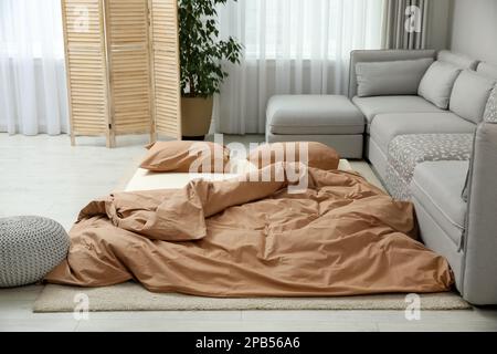 Mattress with pillows and blanket on floor near sofa. Additional sleep place for guest Stock Photo