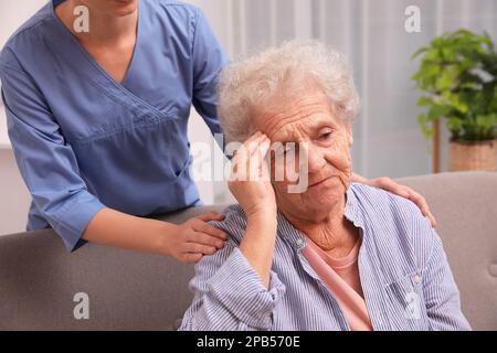 Nurse taking care of senior woman with headache indoors Stock Photo