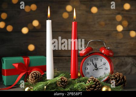 Burning candles, festive decor, gift box and alarm clock on wooden table against blurred Christmas lights Stock Photo