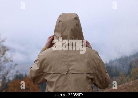 Woman in raincoat enjoying mountain landscape under rain, back view Stock Photo