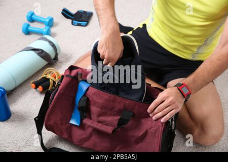 Man packing sports stuff for training into bag on floor indoors, closeup Stock Photo