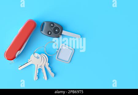 Metal keys bunch, an empty plate for the text or logo, a red folding knife and a car keychain key, with black buttons. Car key cover on blue table. Stock Photo
