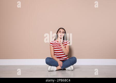 Young woman sitting on floor near beige wall indoors Stock Photo