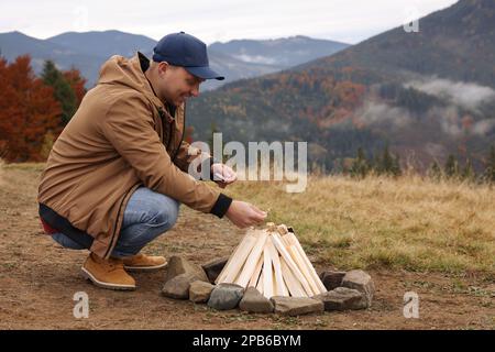 Young man making bonfire in mountains. Camping season Stock Photo