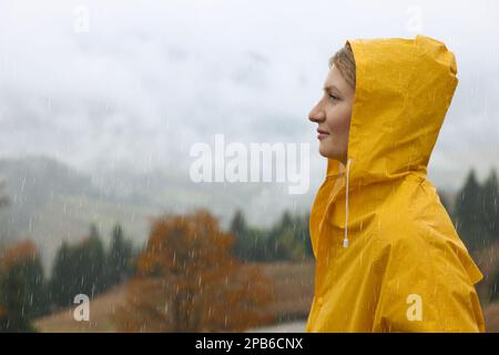 Young woman in raincoat enjoying mountain landscape under rain Stock Photo