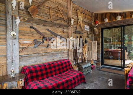 Old piece sur piece log wall decorated with antique objects and sofa with red and black checkered blanket in sunroom inside hybrid timber frame home. Stock Photo