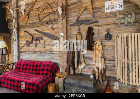 Old piece sur piece log wall decorated with antique objects and sofa with red and black checkered blanket in sunroom inside hybrid timber frame home. Stock Photo