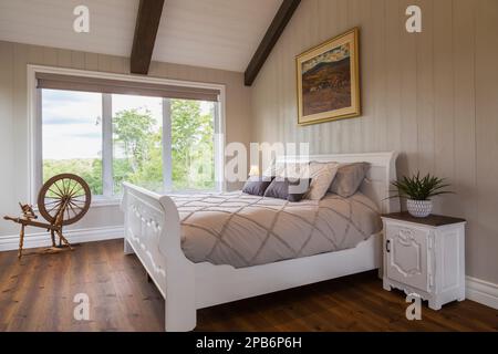 White painted king size sleigh bed in main bedroom with brushed wood plank walls and red pine wood floorboards inside hybrid timber frame home. Stock Photo