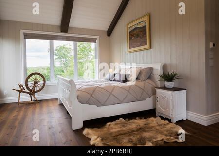 White painted king size sleigh bed in main bedroom with brushed wood plank walls and red pine wood floorboards inside hybrid timber frame home. Stock Photo