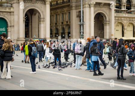 MILAN, ITALY - APRIL 2022: A group of people having fun, taking pictures and feeding the pigeons on the Cathedral Square or Piazza del Duomo in the ce Stock Photo