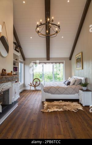 White painted king size sleigh bed in main bedroom with decorative fireplace, brushed wood plank walls, red pine wood floorboards inside timber home. Stock Photo