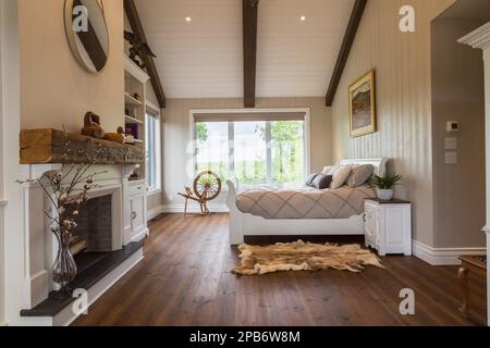 White painted king size sleigh bed in main bedroom with decorative fireplace, brushed wood plank walls, red pine wood floorboards inside hybrid timber Stock Photo