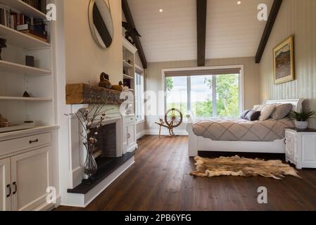 White painted king size sleigh bed in main bedroom with decorative fireplace, brushed wood plank walls, red pine wood floorboards inside timber home. Stock Photo