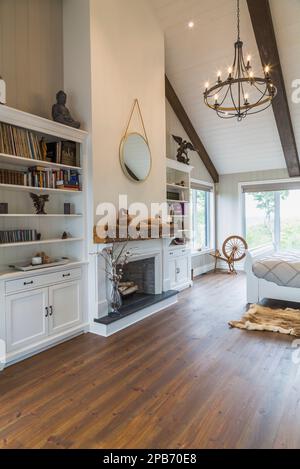 White painted king size sleigh bed in main bedroom with decorative fireplace, brushed wood plank walls, red pine wood floorboards inside timber home. Stock Photo