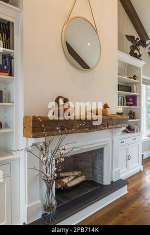 White painted decorative fireplace between bookcases and red pine wood floorboards in main bedroom inside hybrid timber frame home. Stock Photo
