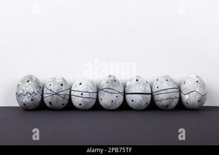 Seven grey Easter eggs in a black pattern on a grey background. Stock Photo