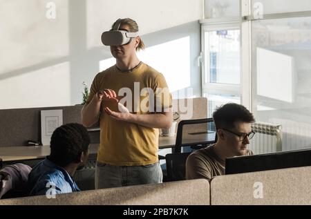 IT Development Team Working on VR Project. Man wearing VR headset, playing and touching something in the virtual world. Diverse men programmers using Stock Photo