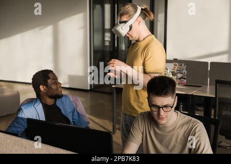 IT Development Team Working on VR Project. Man wearing VR headset, playing and touching something in the virtual world. Diverse men programmers using Stock Photo
