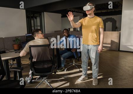 IT Development Team Working on VR Project. Man wearing VR headset, playing and touching something in the virtual world. Diverse men programmers using Stock Photo
