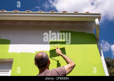 A man painting a house in green at the eco-village of Loural in the mountains of central Portugal. Here, the Klein family and their partners have been working on an ambitious project to rehabilitate a small village that has been abandoned since the year 2000 into an eco-location. On 30 hectares, the aim is to improve the ecosystem by practicing organic agriculture, reforestation and the production of green energy. The small stone village is moving towards food and energy autonomy and its vegetation is gradually coming back to life. The place is starting to provide integrative health training a Stock Photo