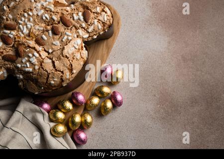 Easter dove cake with almond, chocolate Easter eggs, wooden cutting board, striped beige napkin on concrete background, place for recipe, copy space, Stock Photo