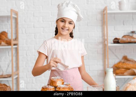 Little baker sprinkling sugar powder onto buns in kitchen Stock Photo