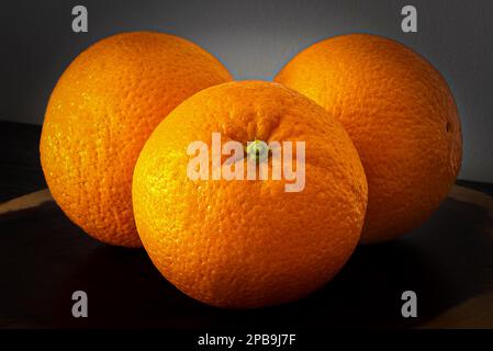 Fresh fragrant oranges on a wooden stand. Three fruits full of vitamin C for health. Stock Photo